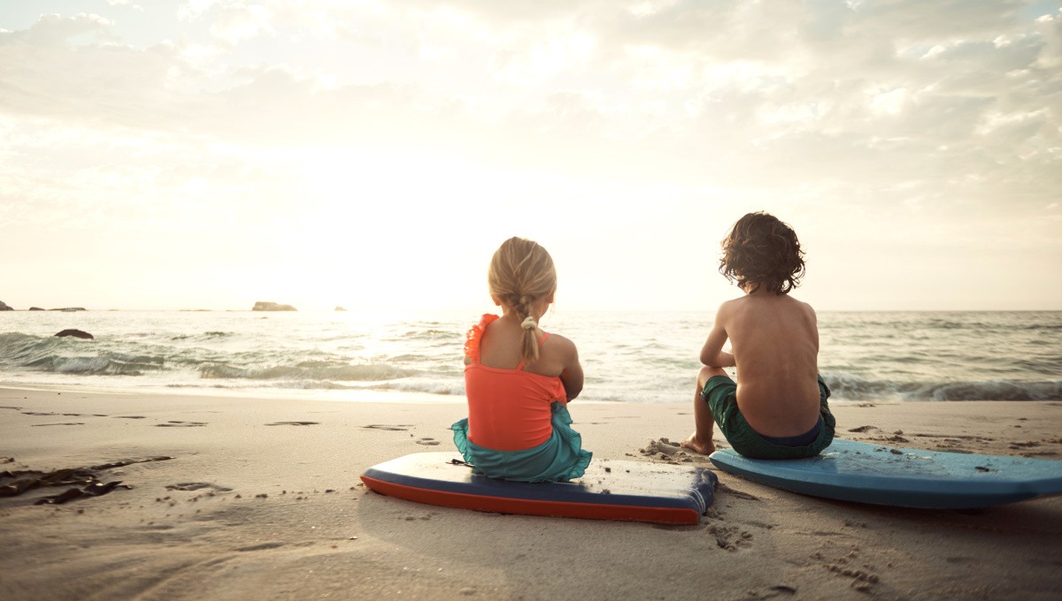 Zwei Kinder sitzen mit Bodyboards am Strand Zwei Kinder sitzen mit Bodyboards am Strand