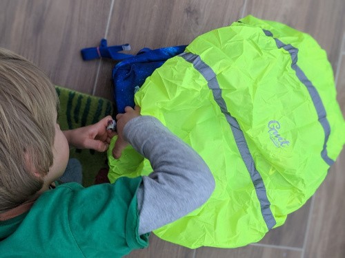 Kind zieht Regencover über Schulranzen