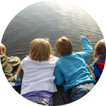 Vier Kinder liegen bäuchlings auf Steg am See