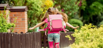 Mädchen mit rosa Schulranzen rennt einen Weg entlang