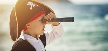 Als Pirat verkleideter Junge mit Fernrohr am Meer