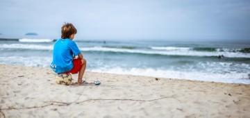 Junge sitzt auf Ball am Meer