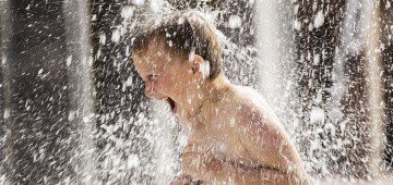 Junge unter Wasserfontäne Junge unter Wasserfontäne