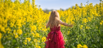 Mädchen in rotem Kleid im gelben Rapsfeld