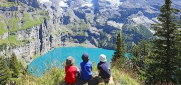 Drei Kinder sitzen oberhalb eines Bergsees