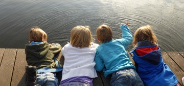 Vier Kinder liegen bäuchlings auf Steg am See