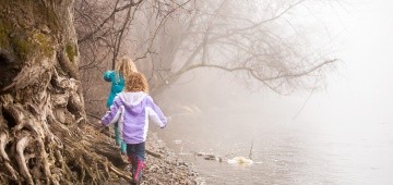 Zwei Mädchen laufen im Nebel am Fluss entlang