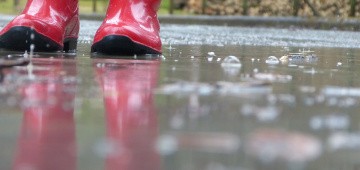 Rote Gummistiefel in Regenpfütze Rote Gummistiefel in Regenpfütze