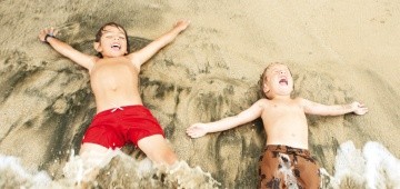 Zwei Kinder liegen am Strand im Spülsaum