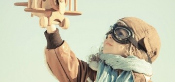 Junge mit Fliegerbrille hebt Spielzeugflugzeug in die Luft