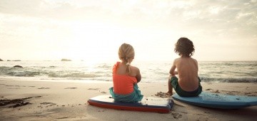 Zwei Kinder sitzen mit Bodyboards am Strand