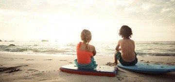 Zwei Kinder sitzen mit Bodyboards am Strand Zwei Kinder sitzen mit Bodyboards am Strand